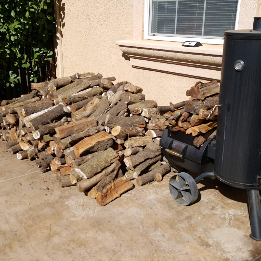 Stack of firewood next to a black barbecue smoker on a concrete patio in Fairfield CA.