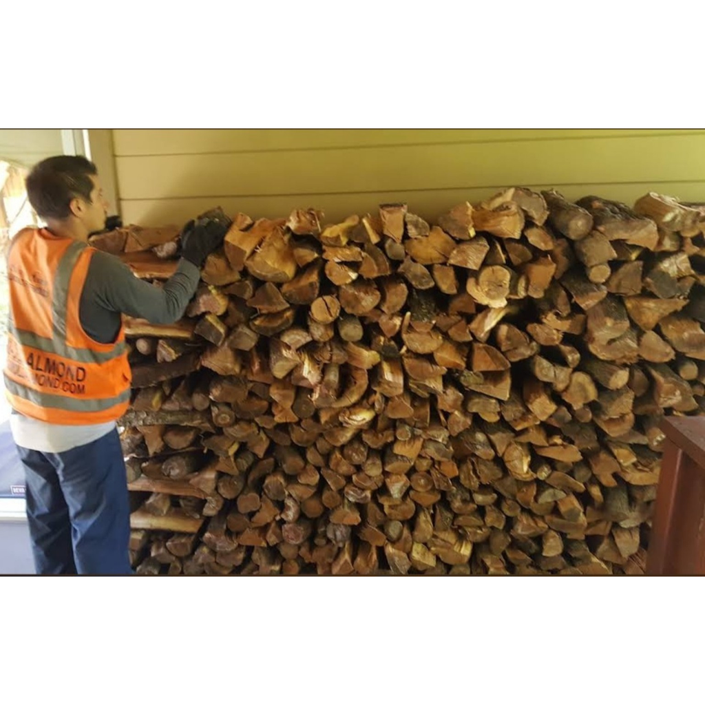 Person in an orange safety vest arranging stacked almond firewood in Oakland CA.