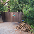 Wooden entry gate of home in Scott's Valley Ca with a pile of almond firewood logs in driveway surrounded by trees.
