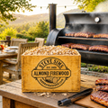 Wooden firewood box labeled 'Steve Sims Almond Firewood' with a grill in the background.