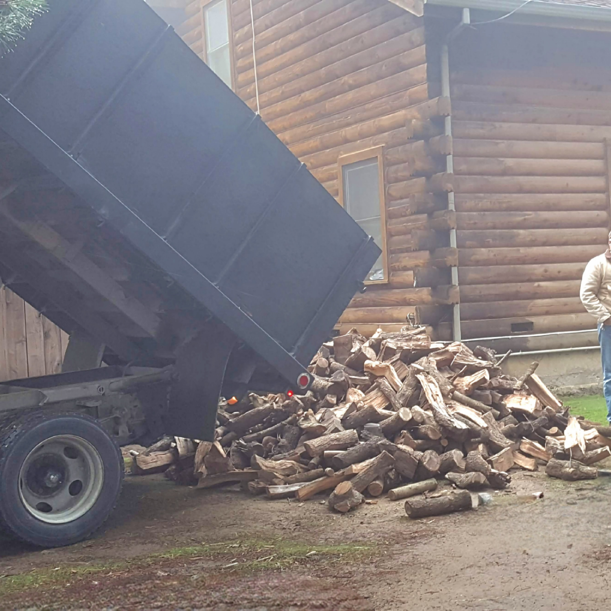 Truck unloading logs onto a pile of almond firewood in driveway of a wooden cabin in Fairfield Ca. 