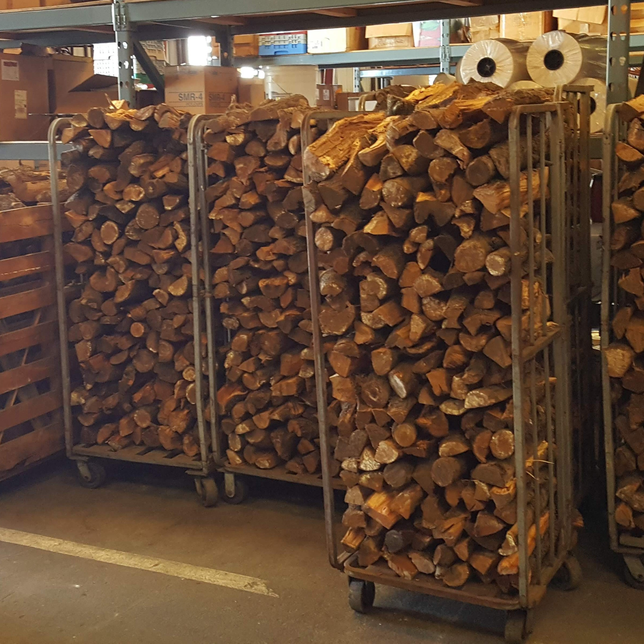 Stacks of firewood on metal carts in a warehouse setting