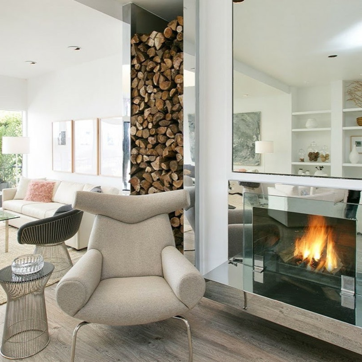 Modern living room with a fireplace, armchair, and stacked firewood.