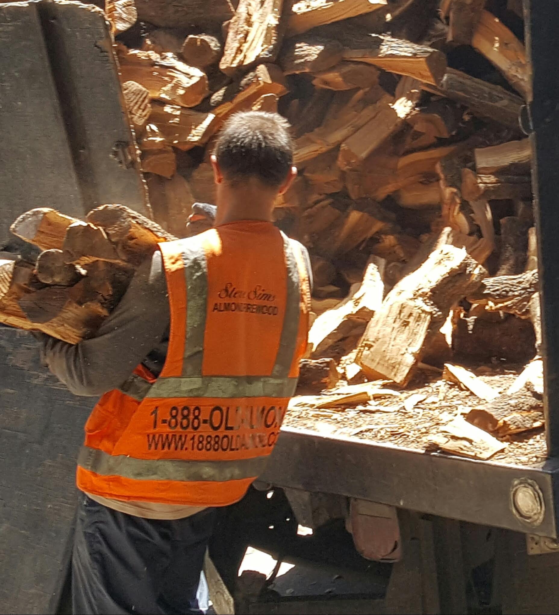 Person in an orange safety vest carrying firewood near delivery truck.