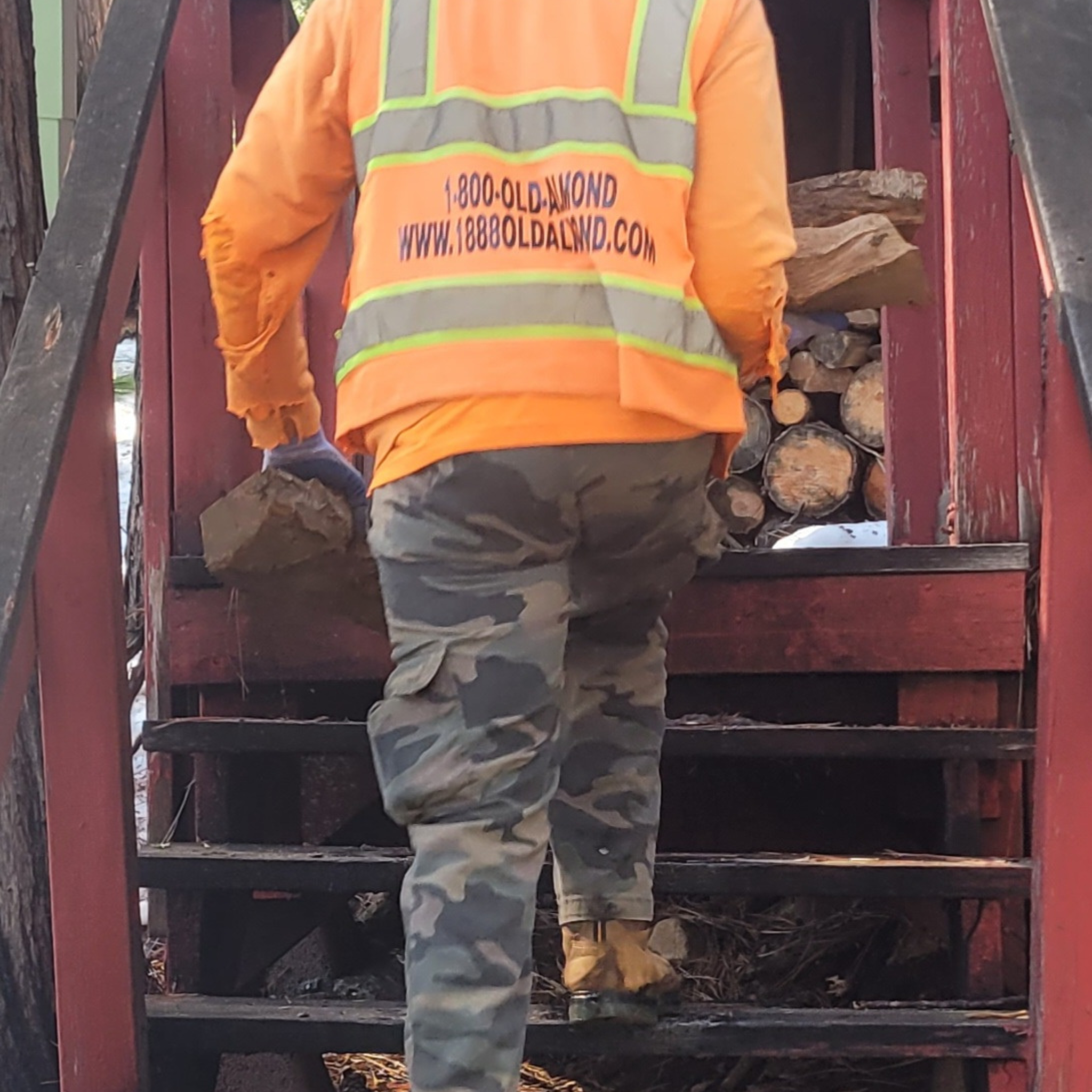 Person in orange safety vest and camouflage pants carrying logs up stairs
